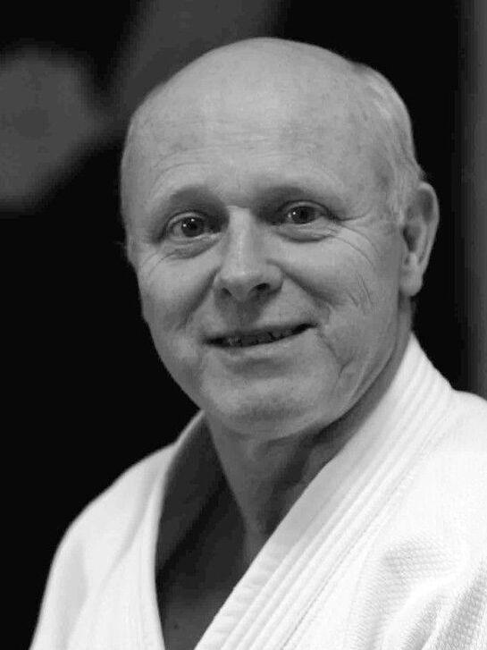 L&auml;chelnder &auml;lterer Mann in Judokleidung, Hintergrund unscharf, freundlicher Ausdruck.
