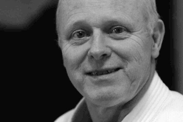 Lächelnder älterer Mann in Judokleidung, Hintergrund unscharf, freundlicher Ausdruck.