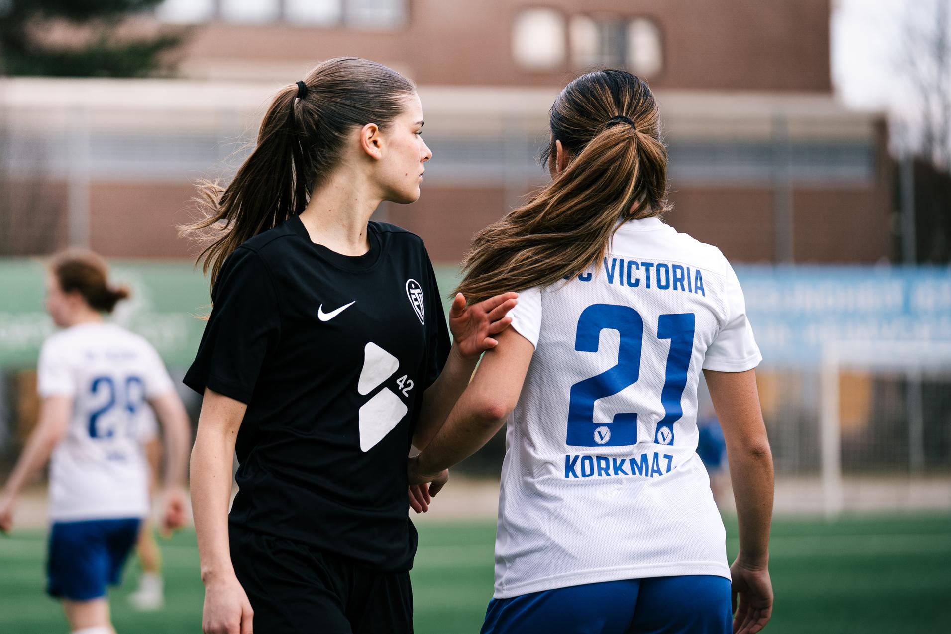 Zwei Fu&szlig;ballspielerinnen im Wettkampf, eine in schwarzem Trikot, die andere in wei&szlig; mit der Nummer 27.