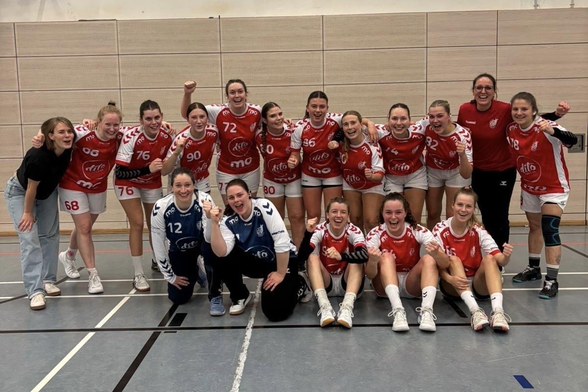 Gruppenfoto eines weiblichen Handballteams in roten Trikots, einige Spielerinnen jubeln, andere l&auml;cheln in die Kamera.