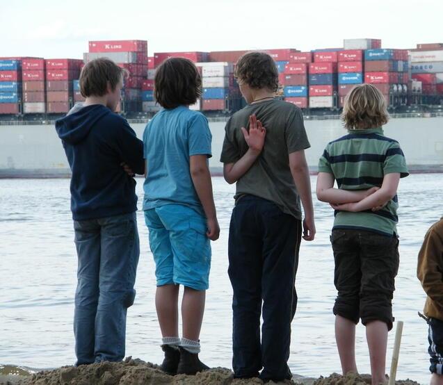 Kinder schauen am Strand auf ein Containerschiff