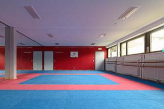 Zwei Trainingsräume: links mit blauer Matte und roten Wänden, rechts mit hellem Holzfußboden und großen Spiegeln.