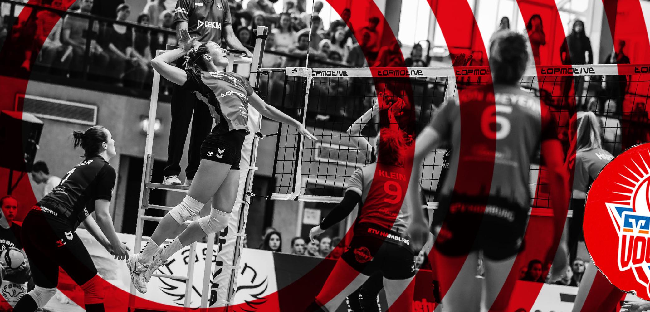 Spielszene aus einem Volleyballspiel: Spielerinnen springen hoch, um den Ball zu schlagen, Zuschauer im Hintergrund.
