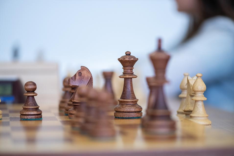 Nahaufnahme eines Schachbretts mit Holzfiguren, darunter ein Bauer und ein Springer in Bewegung.