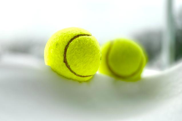 Nahaufnahme von zwei gelben Tennisbällen auf einem weißen Tisch. Hintergrund leicht unscharf.